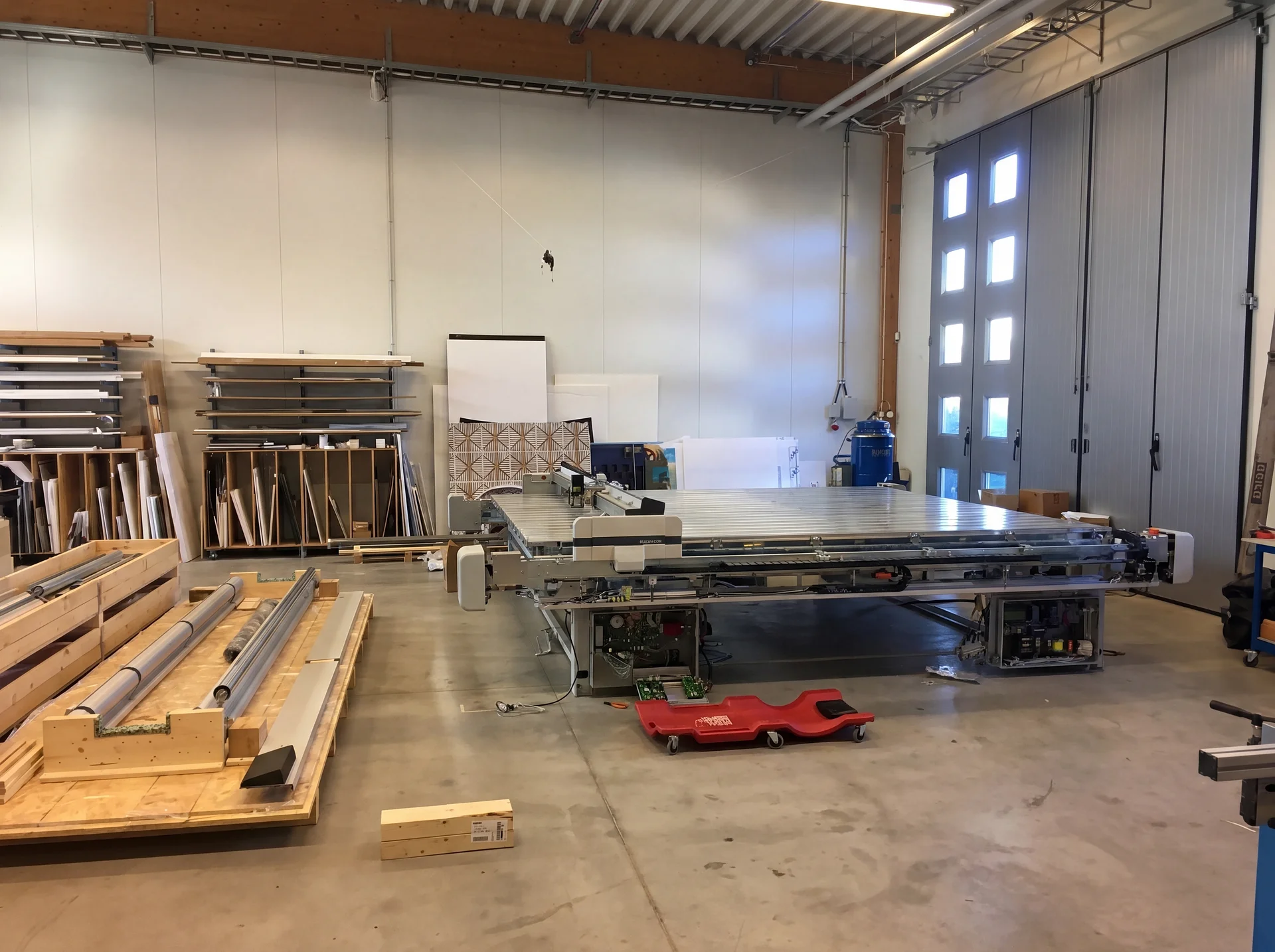 Snickeriverkstad med CNC-maskin, trämaterial och verktyg på betongolv.